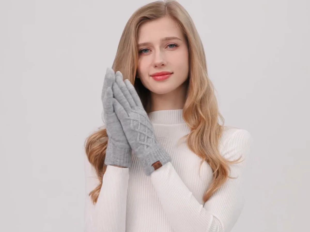 A frosted window wiped clear to show a woman warming her hands in grey REACH STAR diamond-knit touchscreen gloves
